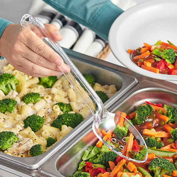 A hand holding a Visions clear plastic slotted serving spoon over a bowl of food.