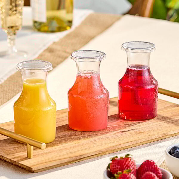 A wooden tray holding glass carafes of juice with berries on top.