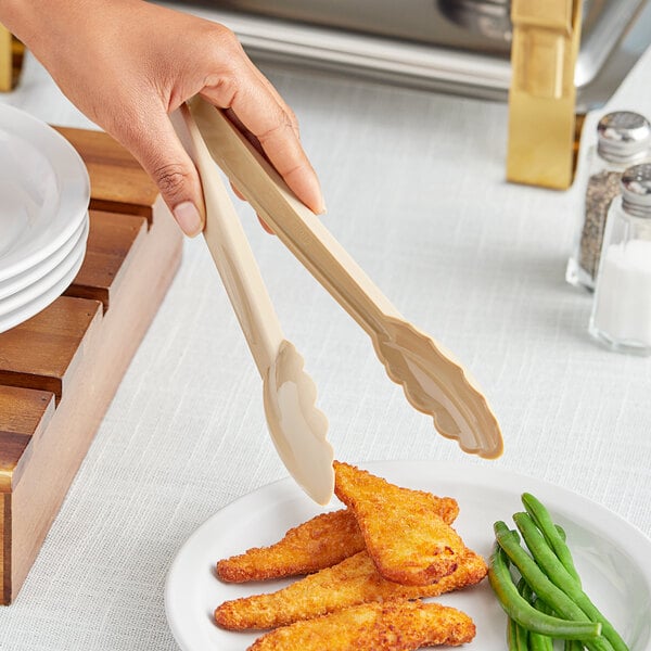 A person holding a pair of beige Choice polycarbonate scallop grip tongs over a plate of food.