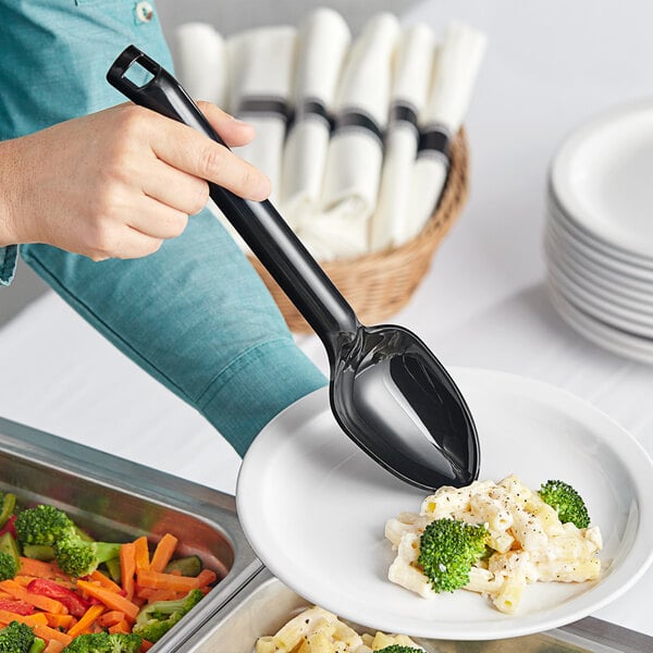 A person holding a black Visions plastic serving spoon over a plate of food.