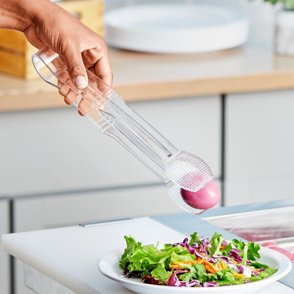 A person using Choice clear polycarbonate tongs to serve salad on a plate.