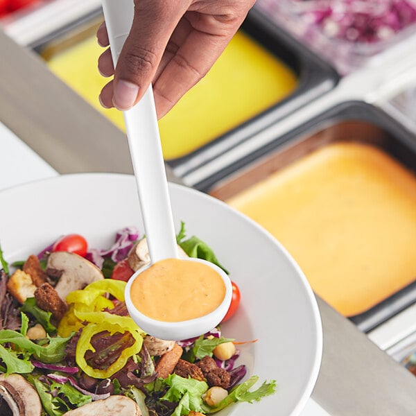 A person using a Choice white polycarbonate serving ladle to scoop salad from a bowl.