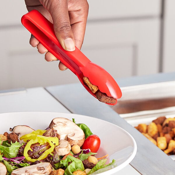 A person holding a Choice red polycarbonate scallop grip tong over a bowl of salad.