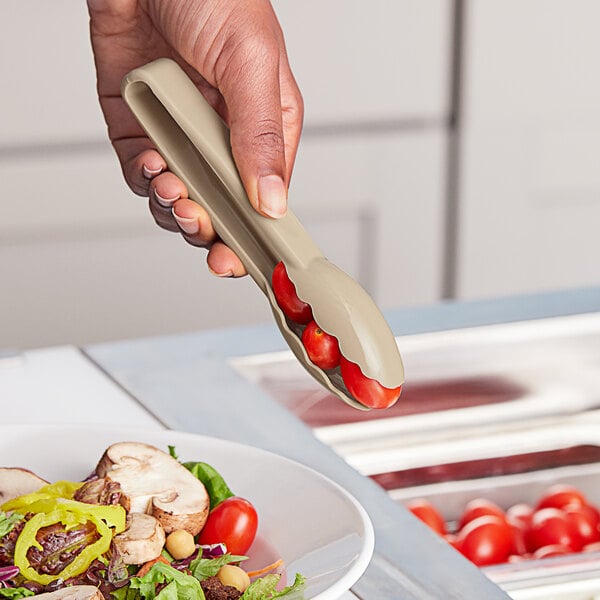 A person using Choice beige scallop grip tongs to serve tomatoes at a salad bar.
