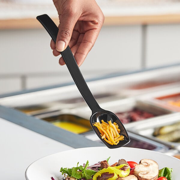 A person holding a Choice black polycarbonate salad bar spoon over a bowl of salad.