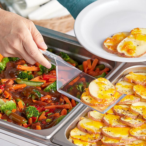 A person holding a clear plastic spatula over food on a plate.