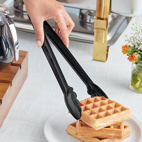 A person using Choice black polycarbonate scallop grip tongs to serve a waffle.