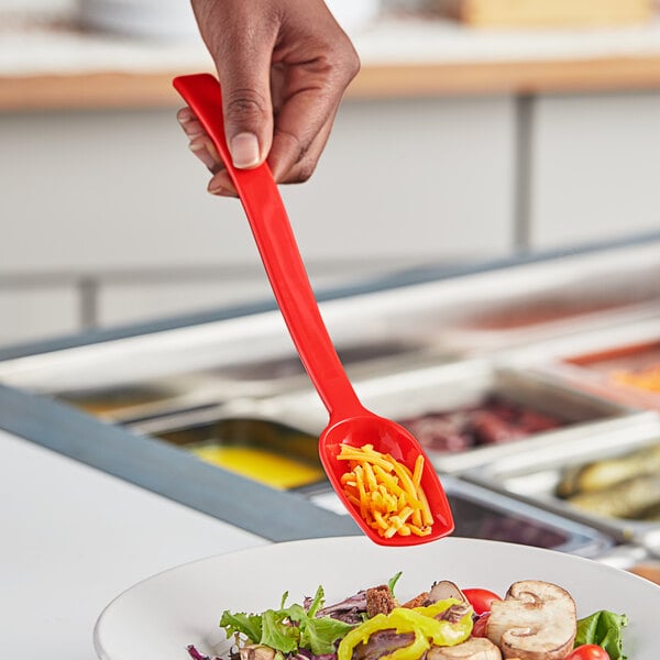 A hand holding a red Choice polycarbonate salad spoon over a salad.