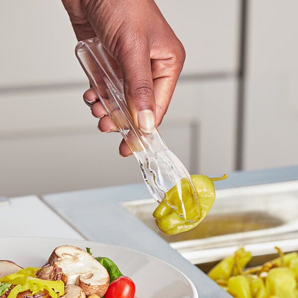 A hand holding clear plastic scallop tongs over a plate of food.