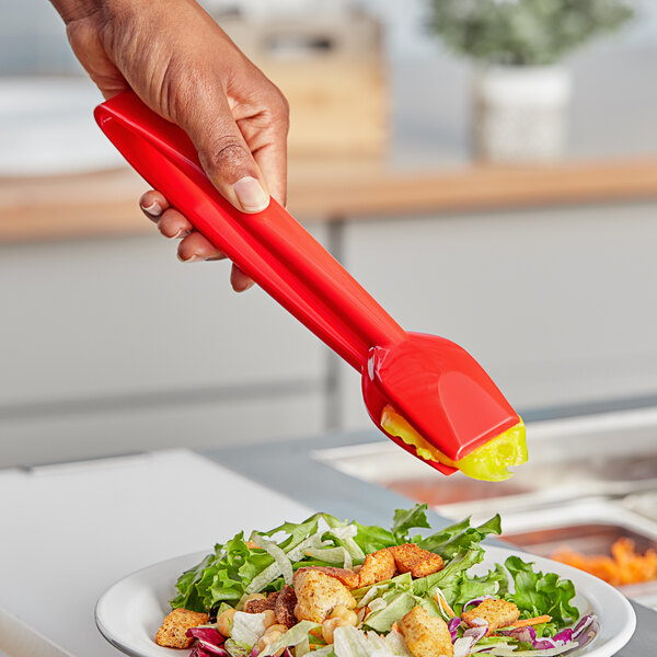 A hand using red Choice salad tongs to serve salad.