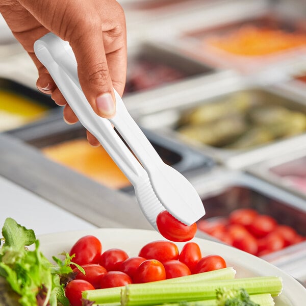 A person holding white Choice flat grip tongs over a salad at a salad bar.