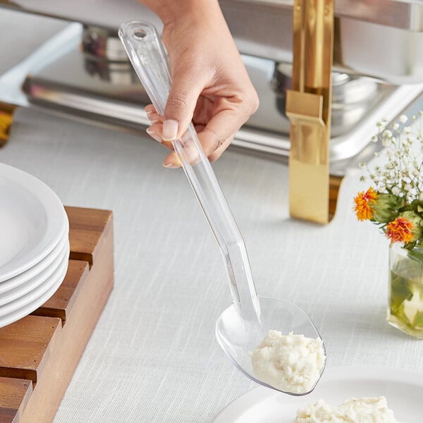 A person using a Choice clear polycarbonate salad bar spoon to serve food on a plate.
