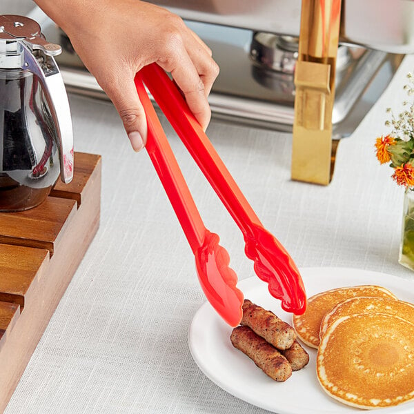 A hand using Choice red polycarbonate tongs to serve pancakes.