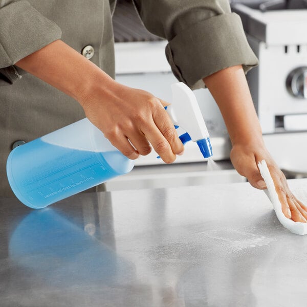 A person in a chef's uniform using a Lavex blue plastic bottle to spray a cleaning product on a counter.