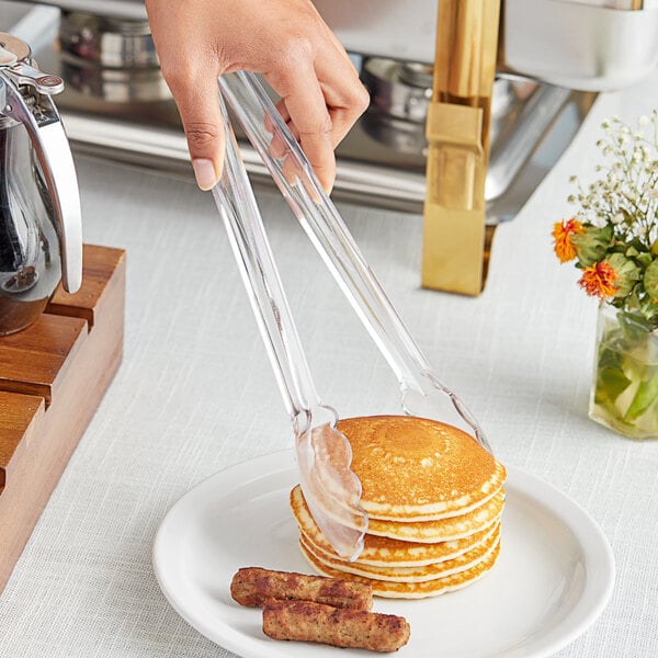A person using Choice clear polycarbonate tongs to serve a stack of pancakes and sausages.