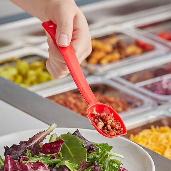 A person holding a red Choice salad bar spoon over a bowl of food.