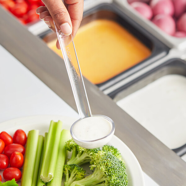 A person using a Choice clear polycarbonate serving ladle to serve broccoli onto a plate.