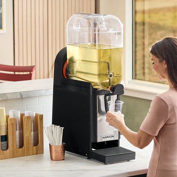 A single-bowl refrigerated beverage dispenser filled with a yellow drink, being used to fill a plastic cup.