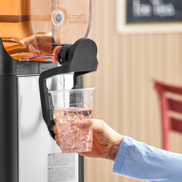 A person dispensing a beverage with ice from a refrigerated beverage dispenser into a clear plastic cup.
