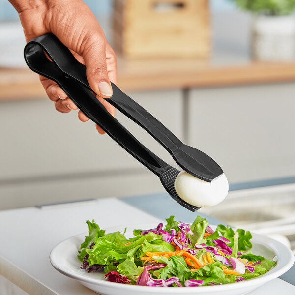 A person using Choice black flat grip tongs to serve a salad