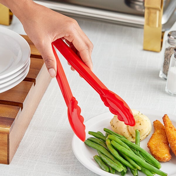 A person using red Choice scallop grip tongs to serve food at a salad bar.