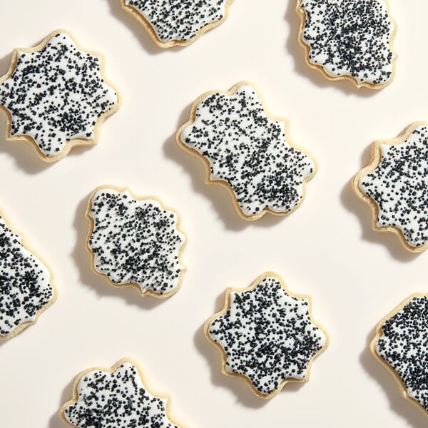A group of cookies with white frosting and black sparkling sugar on top.