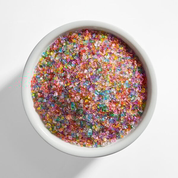 A white bowl filled with coarse, multicolored rainbow sanding sugar crystals.