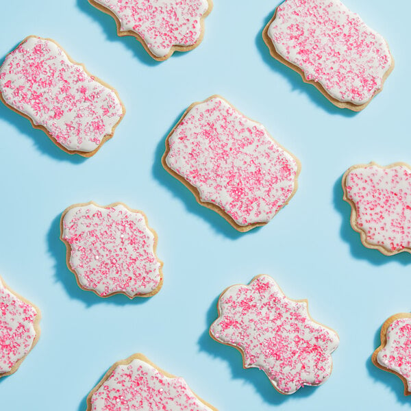 A close up of a cookie with pink frosting and Adourne Pink Sparkling Sugar sprinkles.