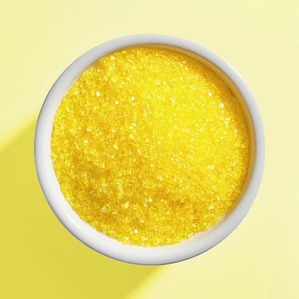 A white bowl filled with coarse yellow sanding sugar.