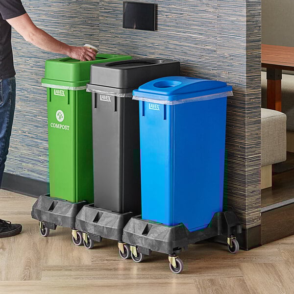 A man standing next to a Lavex 3-stream rectangular trash station with black, green, and blue lids.