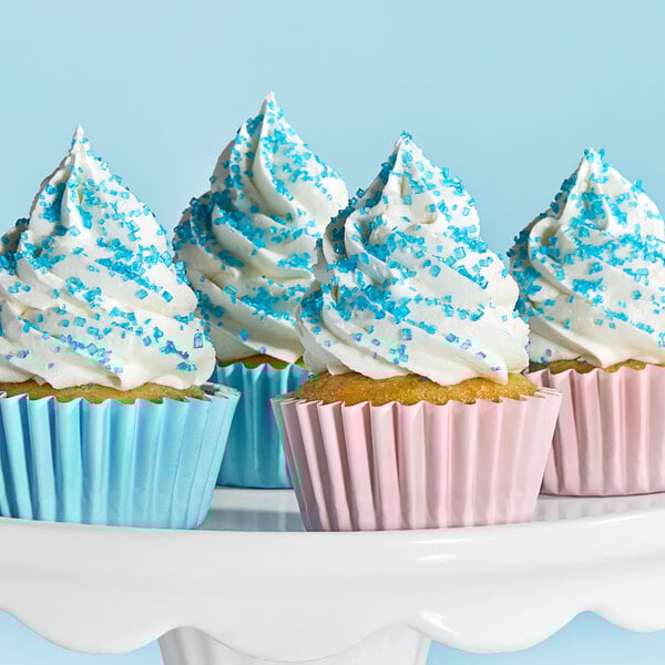 A white cake stand with a cupcake topped with white frosting and blue sprinkles on it.