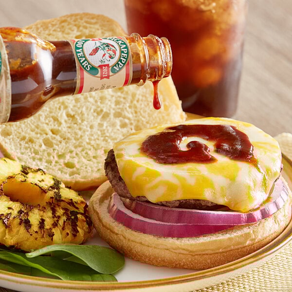 A cheeseburger with onion and Pickapeppa Original Sauce being poured onto it.