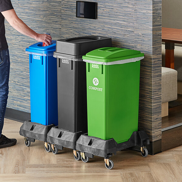 A man standing next to a Lavex 3-stream rectangular trash station with black, green, and blue lids.