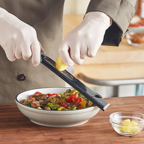 A person using a yellow Microplane 3-in-1 Ginger Grater tool to grate vegetables into a bowl.