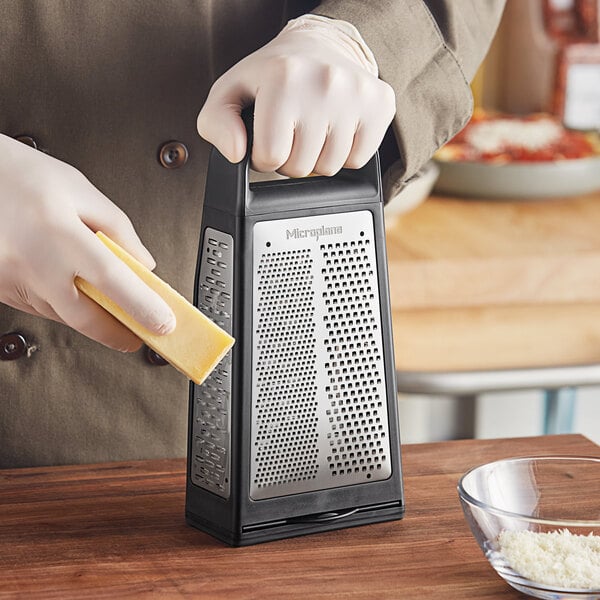 A person using a Microplane Elite stainless steel box grater to grate cheese.