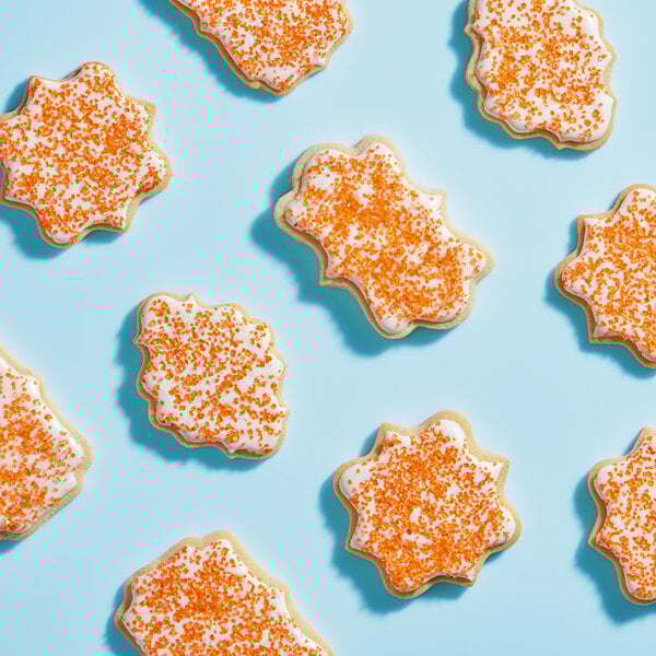 A group of cookies with white frosting and Adourne Orange sparkling sugar.