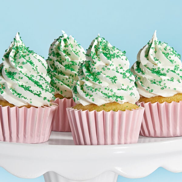 A cupcake with white frosting and Adourne light green sparkling sugar sprinkles.