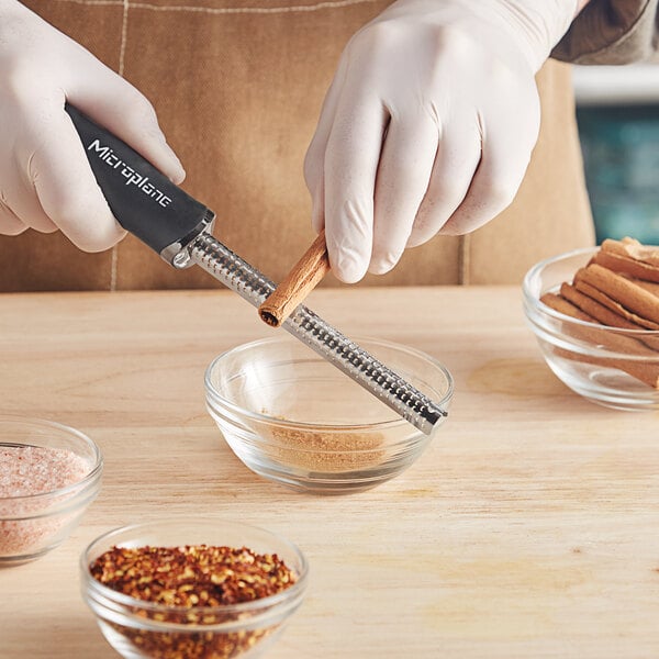 A person in gloves using a Microplane grater to grate spices into a bowl.