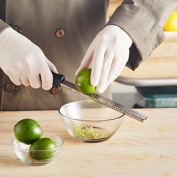 A person grating a lime with a Microplane Classic zester over a bowl.