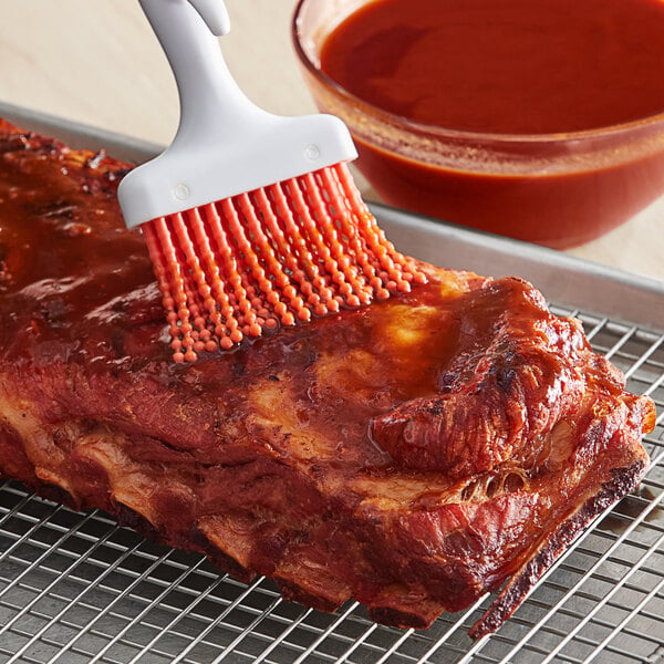 A brush applying red Pickapeppa Spicy Mango sauce to meat.