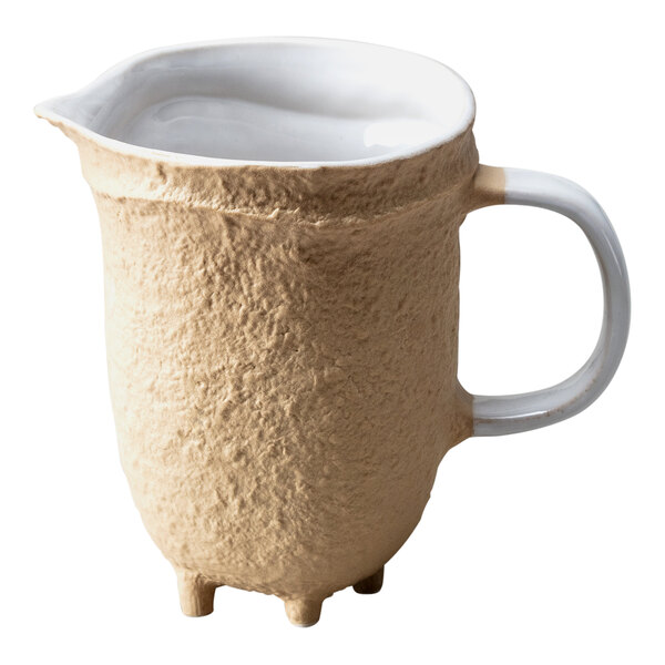 A cream colored Nosse by Fortessa stoneware pitcher with a brown handle.