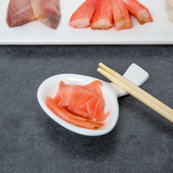 A 10 Strawberry Street Whittier white porcelain spoon with chopstick holder on a bowl of food with chopsticks.