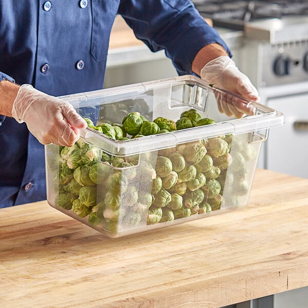 A man in a blue uniform holding a clear polycarbonate food storage container of brussels sprouts.