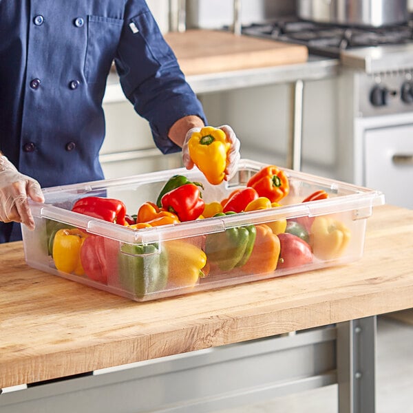 A person holding a Choice clear polycarbonate food storage container of green and yellow bell peppers.