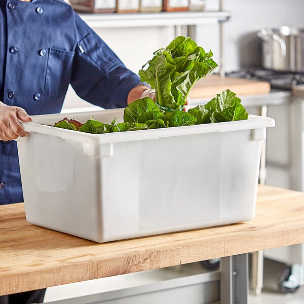 A man in a chef's uniform holding a white Choice food storage container full of green leaves.