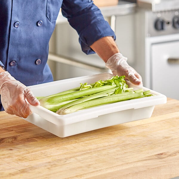 A person holding a white Choice food storage box filled with celery on a wooden surface.