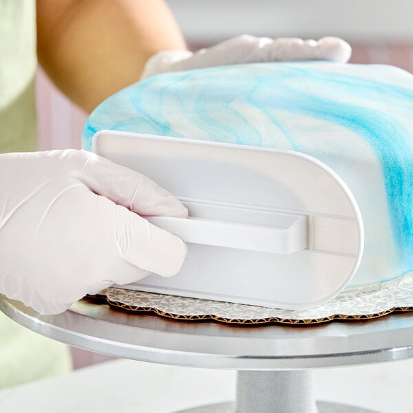 A white plastic fondant smoother being used to smooth blue marbled fondant on a cake.