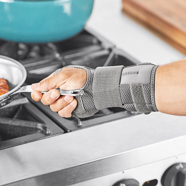 A person wearing a grey 3M Futuro Deluxe wrist stabilizer using a spoon to cook in a pan.