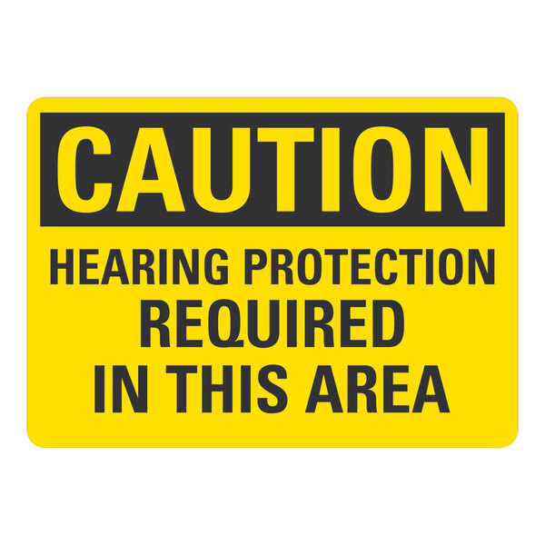 A yellow sign that says "Caution / Hearing Protection Required In This Area" in black letters.