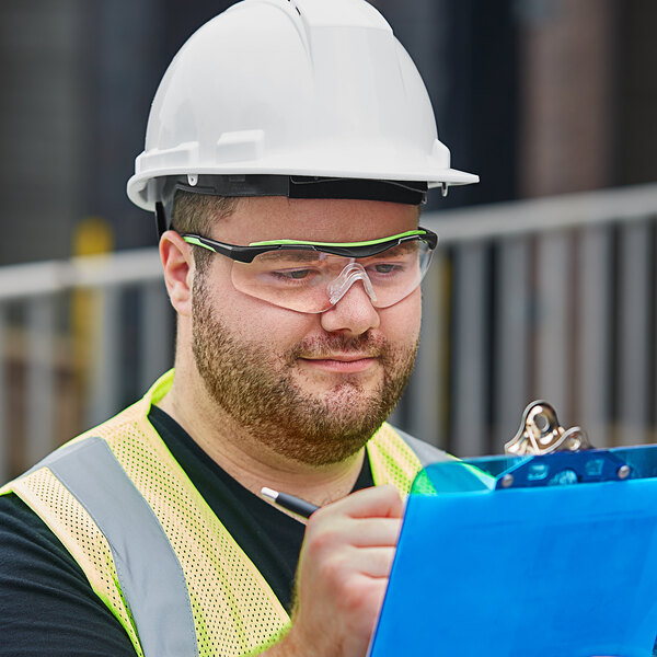 A man wearing a hard hat and 3M Scratch-Resistant Anti-Fog Safety Glasses holding a clipboard.